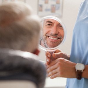 Man smiling at reflection in handheld mirror