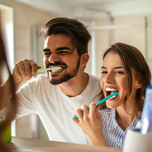Couple smiling while brushing teeth in bathroom