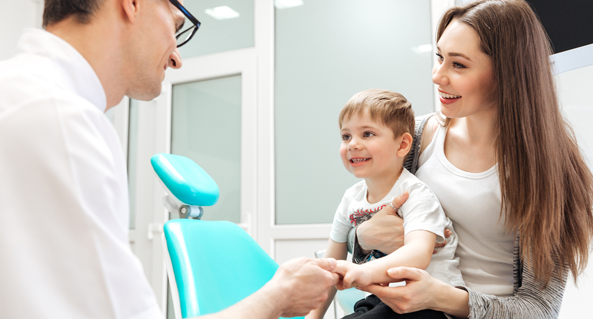 Young boy sitting in his mothers lap and shaking hands with a childrens dentist in Beaverton
