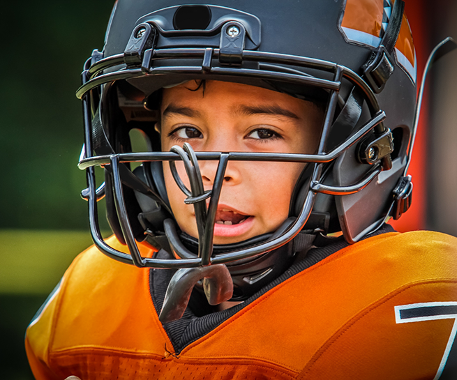 Young boy in a football uniform with a mouthguard hanging from his helmet