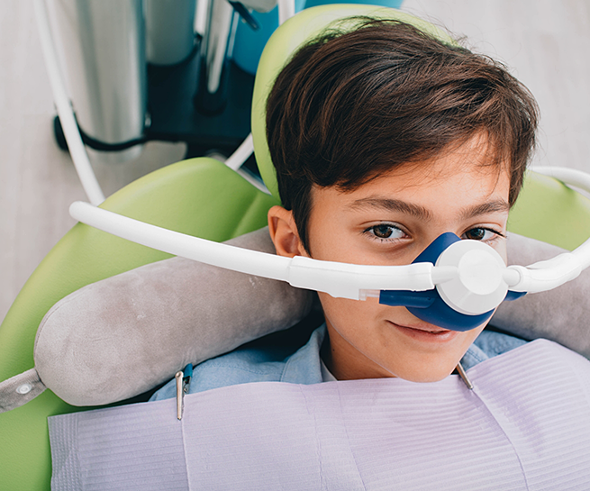 Smiling young boy in dental chair with a nitrous oxide mask over his nose