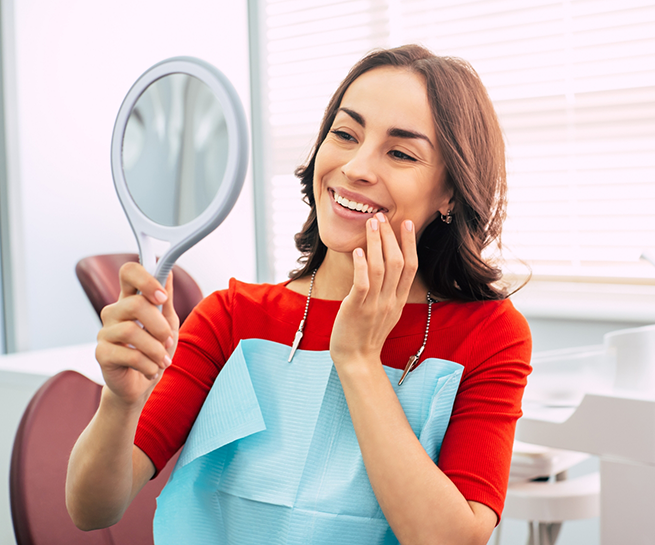 Woman in the dental chair holding a mirror and admiring her smile
