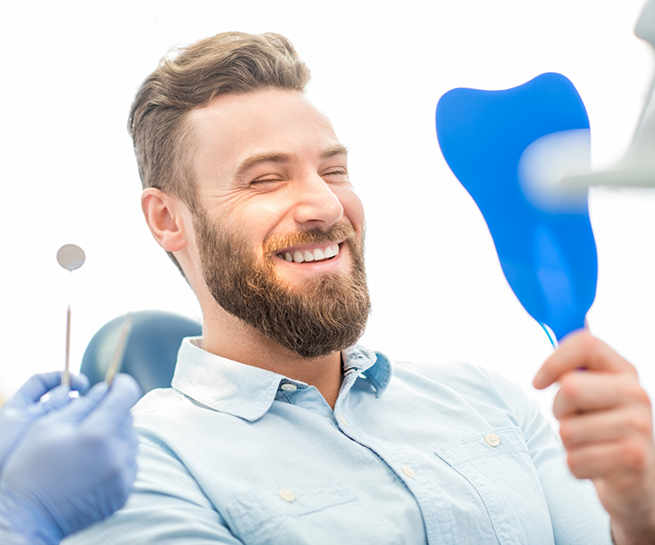 Bearded man in the dental chair admiring his smile in a mirror