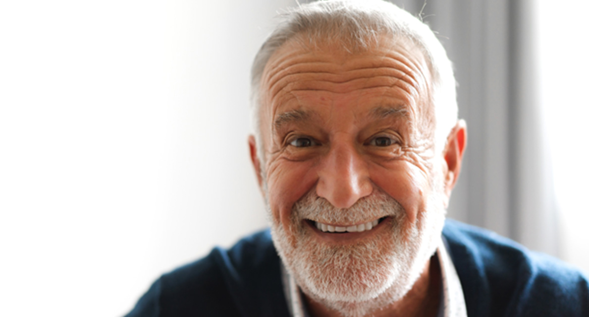 Senior man standing in front of window smiling