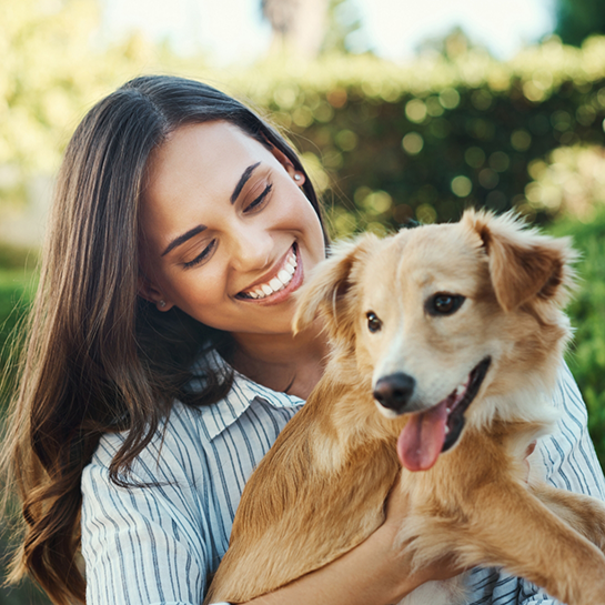 Smiling woman holding a golden fluffy dog outdoors