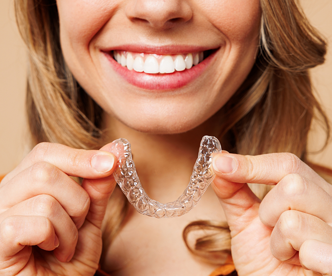 Smiling woman holding an Invisalign aligner near her mouth
