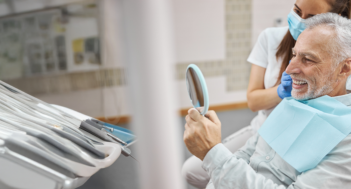 Senior dental patient seeing his smile in a mirror after replacing missing teeth in Beaverton