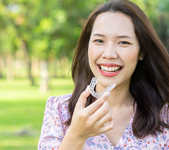 Smiling woman holding a clear aligner outdoors