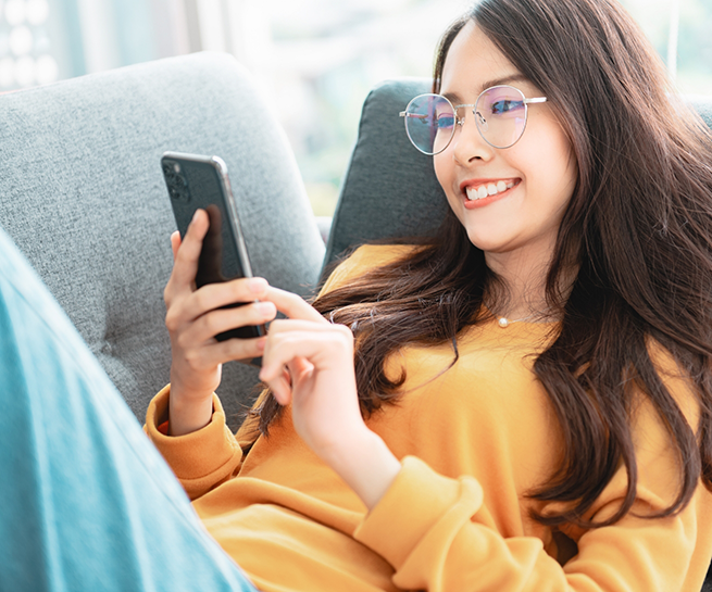 Young woman laying on a couch and smiling while scrolling on her phone