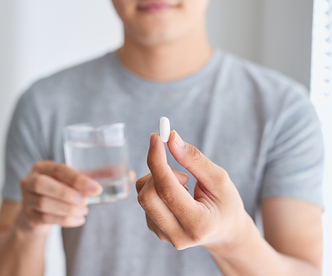 Person holding a white pill and a glass of water