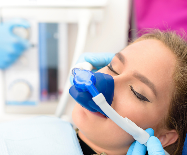 Woman in dental chair with her eyes closed and a nitrous oxide mask over her nose