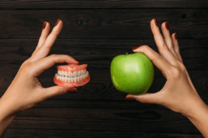 One hand holding dentures while the other holds an apple